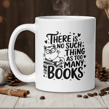 White mug with a cat and book design, text 'There is no such thing as too many books', on a wooden table with coffee beans and a vase in the background.