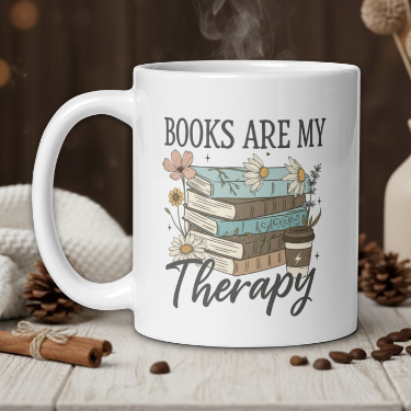 White mug with 'Books are my Therapy' design on a wooden table with coffee beans and a vase in the background.