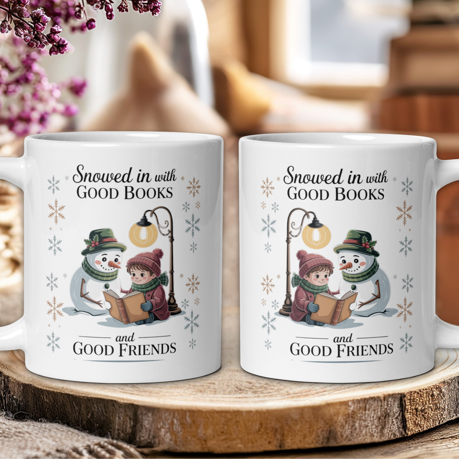 Two mugs with snowman and child illustration and text 'Snowed in with Good Books and Good Friends' on a wooden surface.