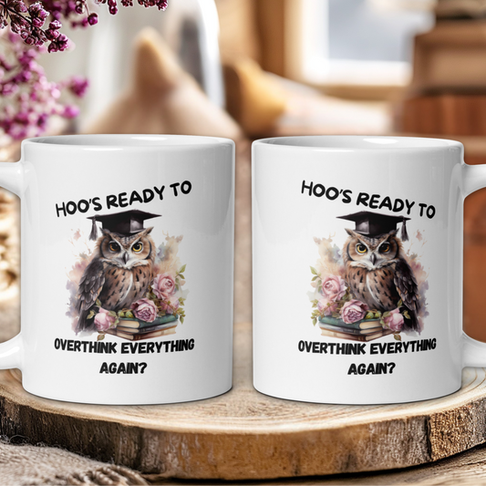 Two white mugs with an owl design and text on a wooden surface.
