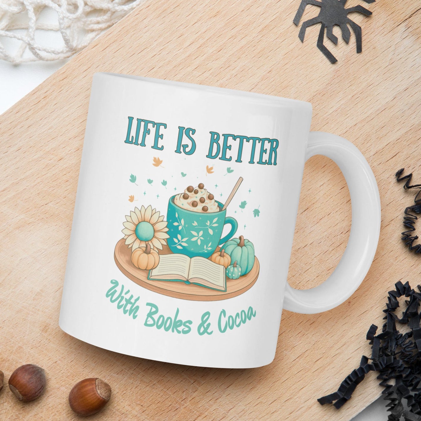 Mug with 'Life is Better with Books & Cocoa' design on a wooden board with nuts and spider decorations.