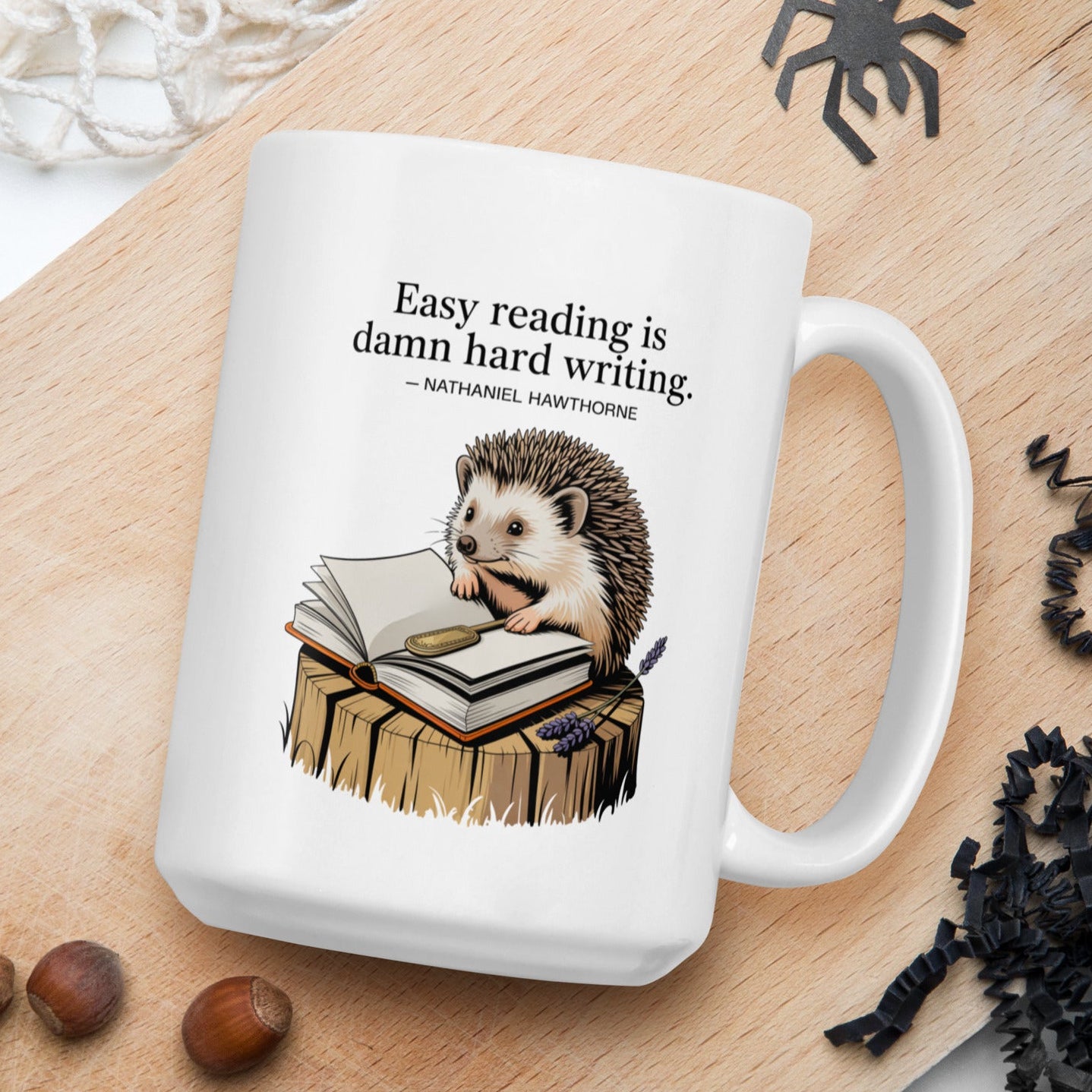 White mug with hedgehog illustration and text on a wooden board with nuts and spider decorations.